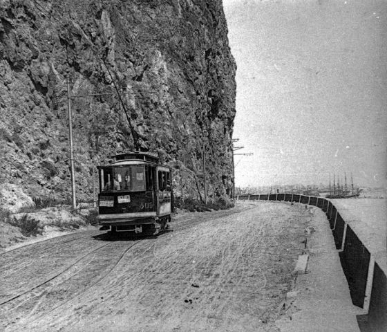Tranvía antiguo circulando junto al acantilado de Montjuïc, con veleros al fondo